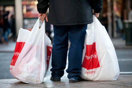 A man carrying two shopping bags waits to cross 6th Avenue on December 26, 2011 in New York City.