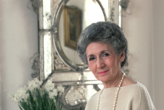 1986: A portrait of architecture critic Ada Louise Huxtable seated on a table next to a sofa with flowers and a mirror in the background. 1986: A portrait of architecture critic Ada Louise Huxtable seated on a table next to a sofa with flowers and a mirror in the background.