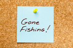 GONE FISHING! written on a blue sticky note on an office cork bulletin board. GONE FISHING! written on a blue sticky note on an office cork bulletin board.