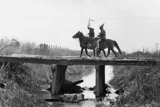ca. 1978, Mamou, Louisiana, USA --- Two costumed Cajun Mardi Gras riders cross a bridge. Mamou, Louisiana. --- Image by ? Philip Gould/Corbis
