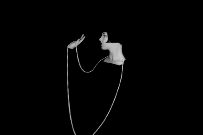 1929: American actress Louise Brooks (1906 - 1985) wearing a long necklace which stands out starkly against a black background. (Photo by Eugene Robert Richee/John Kobal Foundation/Getty Images)