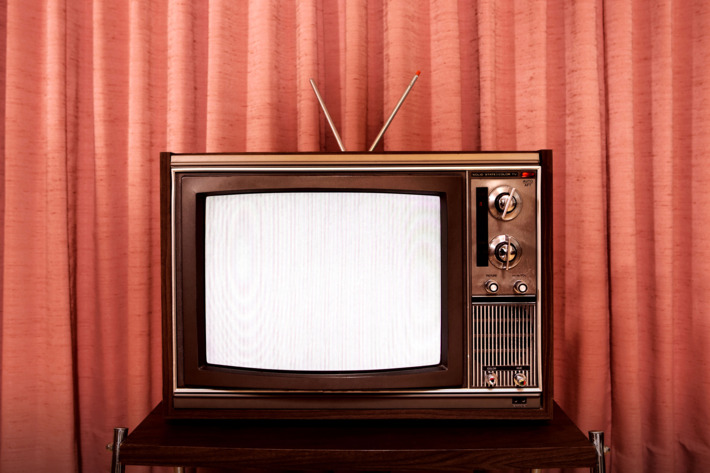 Old television on stand, in front of curtain