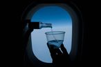 Person pouring whiskey into a glass in front of an airplane window