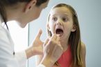 Doctor looking in girl's mouth, using tongue depressor