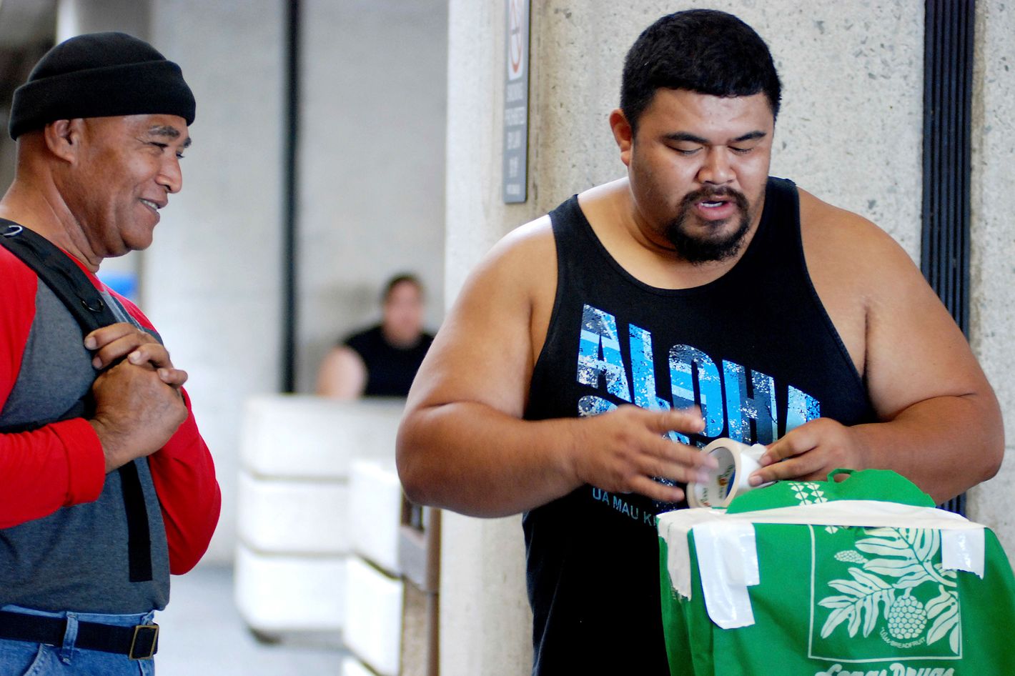 In this Oct. 10, 2016 photo, Mua Migi, left, watches his son Atimua Migi put tape on a carry-on bag before boarding a Hawaiian Airlines flight to Pago Pago, American Samoa at Honolulu International Airport in Honolulu. Atimua Migi doesn't like the airline's new policy of assigning seats at the airport after the airline conducted a survey that involved weighing passengers traveling between Pago Pago and Honolulu. (AP Photo/Jennifer Sinco Kelleher)